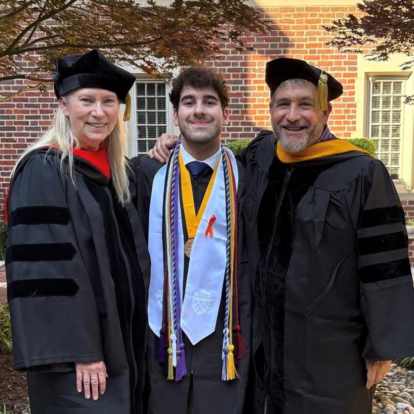 Nick in graduation attire with two people.